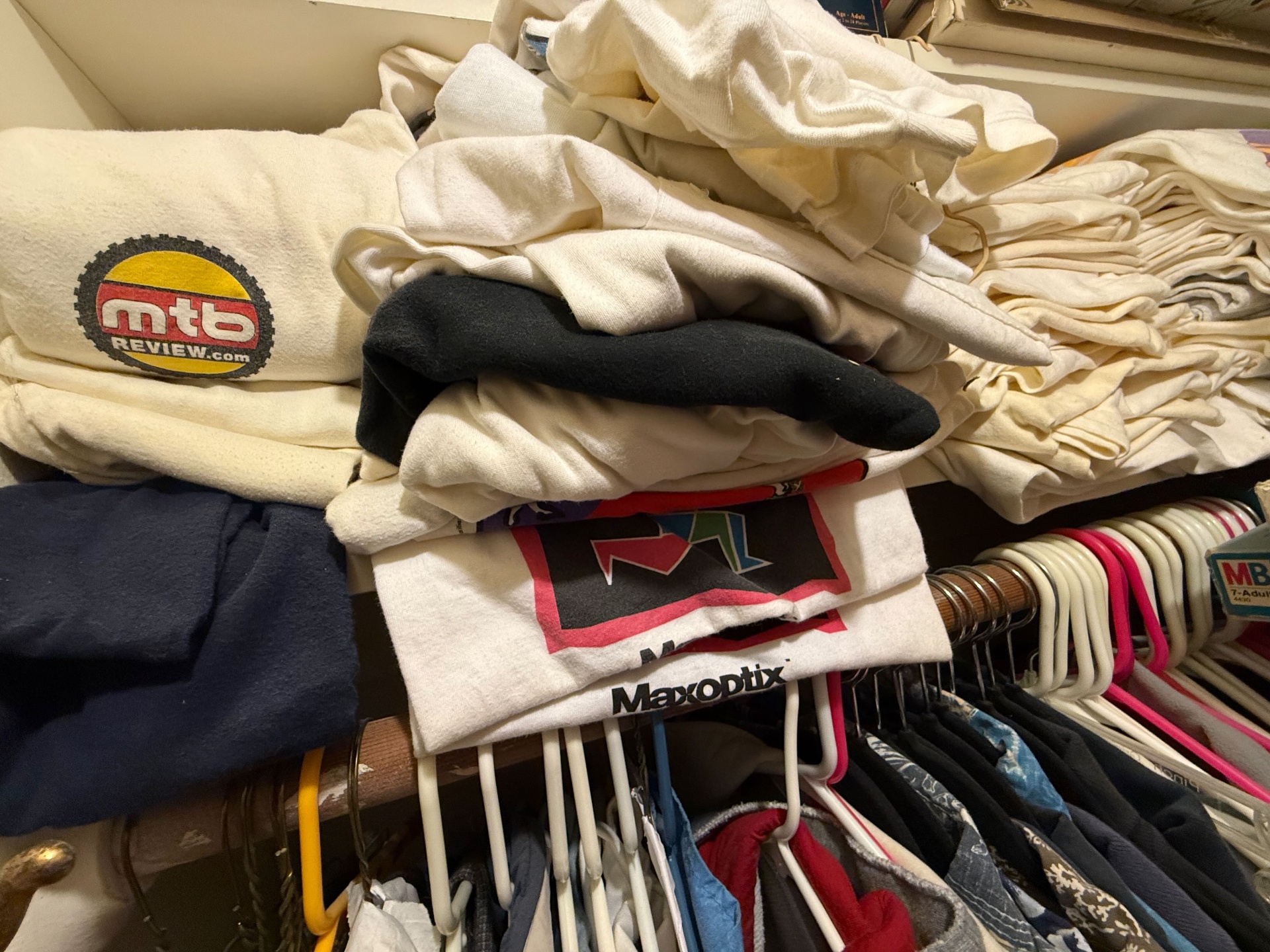 A closet shelf piled high with old tech t-shirts